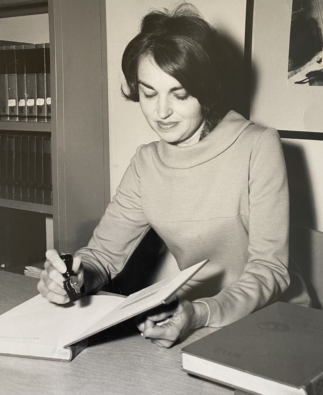 A black and white photo of a woman stamping a library book